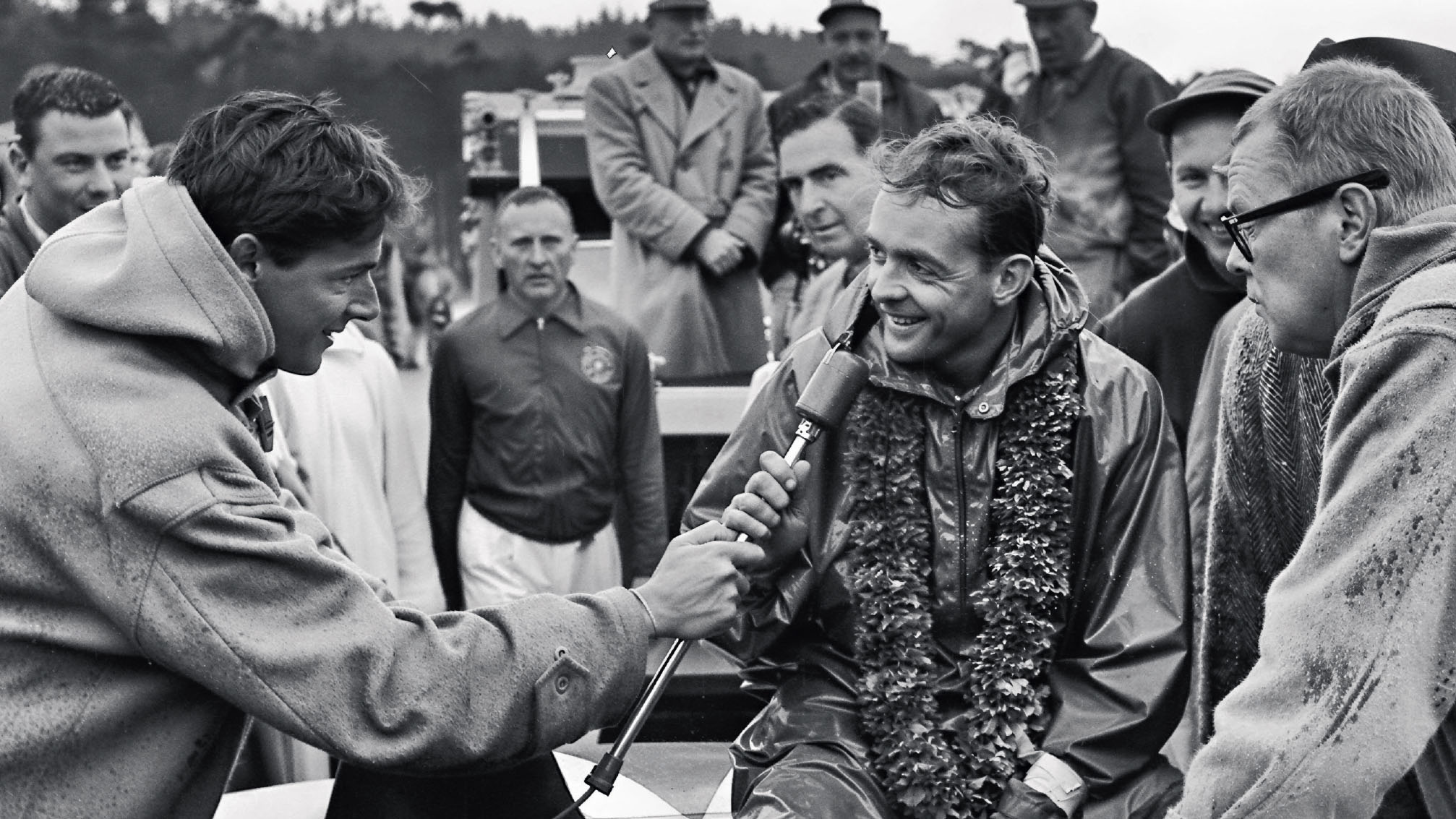 Black and white photograph of a man receiving an award or trophy from another person, with a crowd of people in the background.