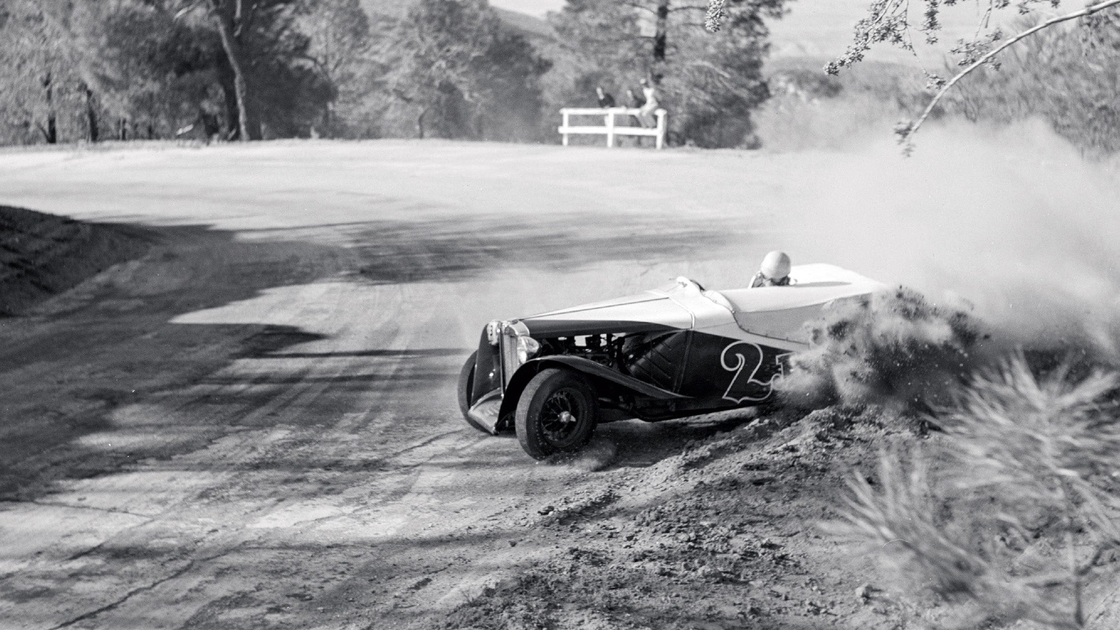 Vintage car racing on a dirt track with trees in the background