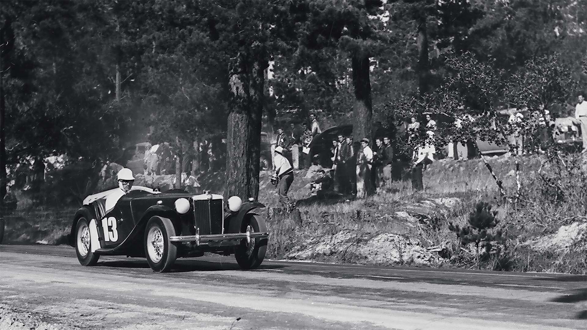 Vintage car racing on a road with spectators in the background