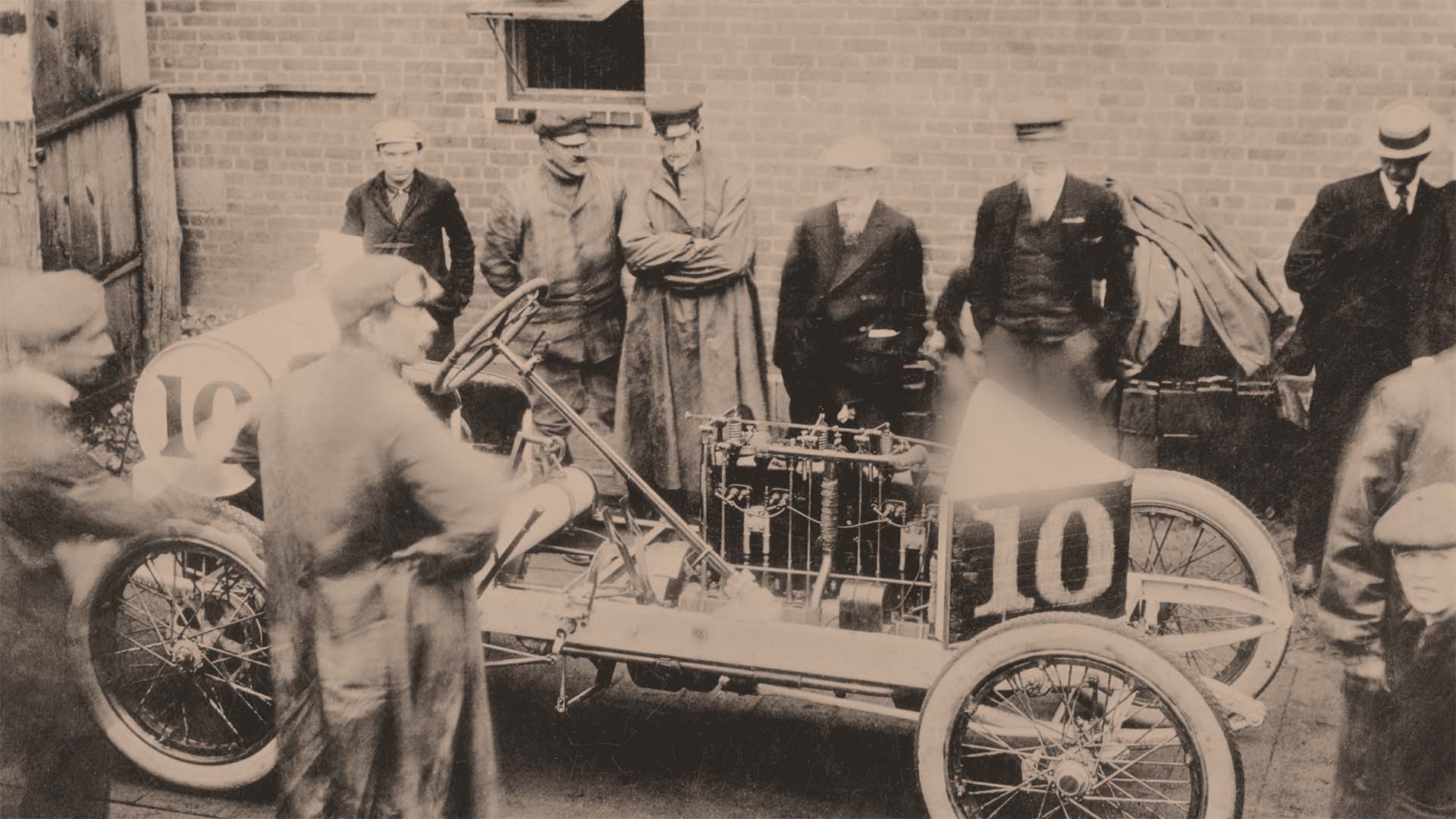 Vintage black and white photograph of a car race with men and cars from the early 20th century.