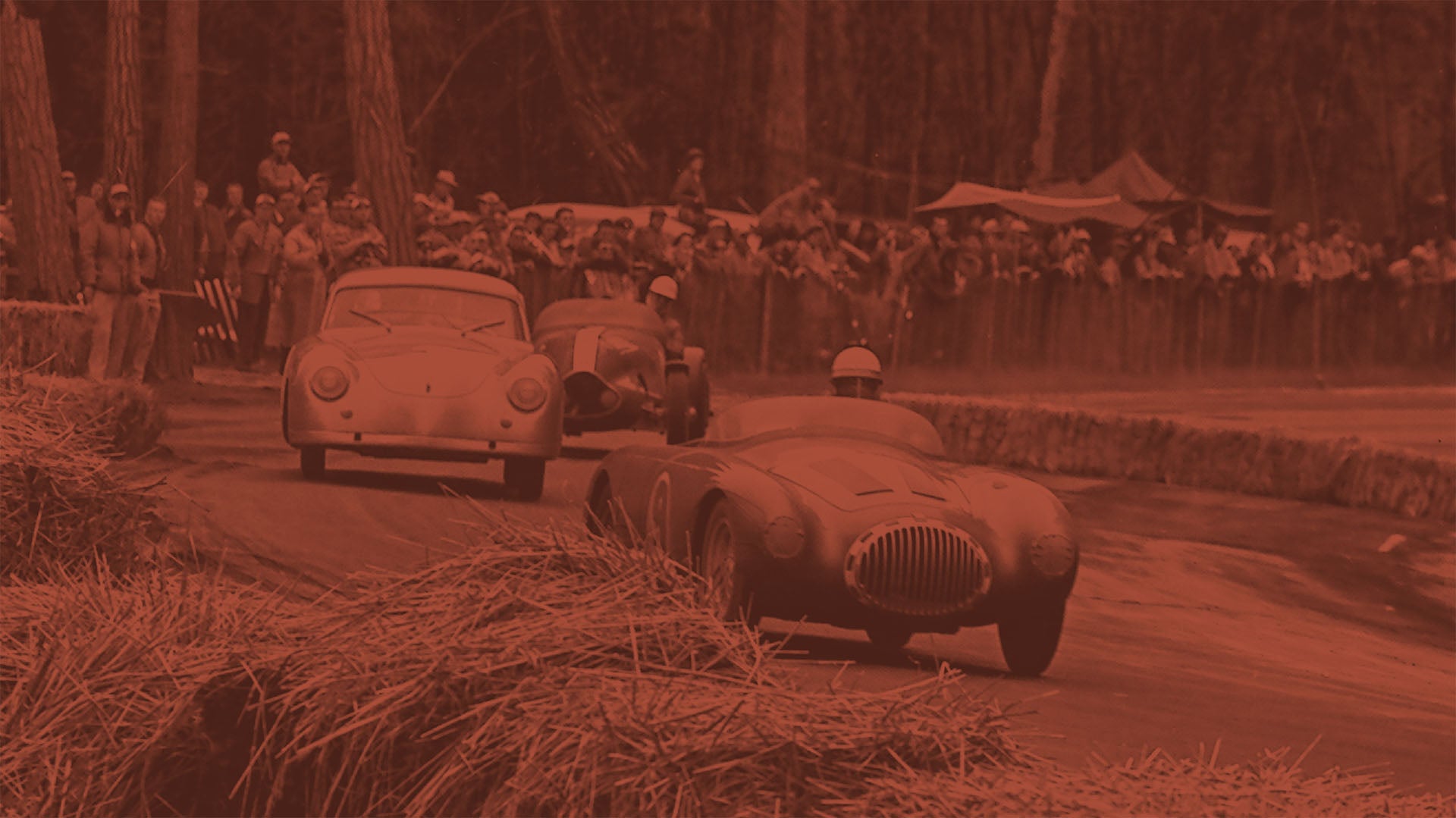 Vintage cars racing on a dirt track with spectators watching.