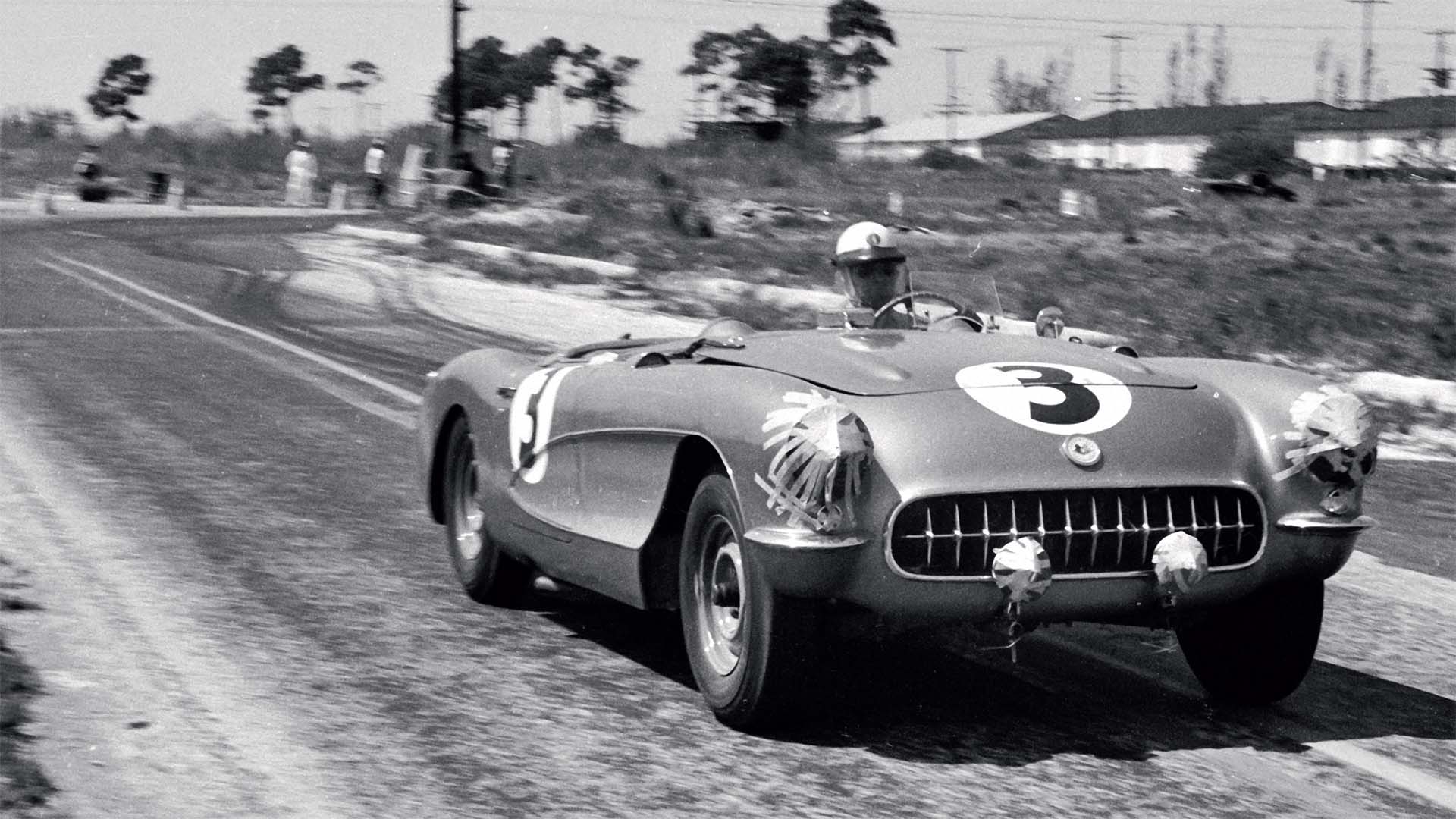 Vintage race car on a track with a driver wearing a helmet.