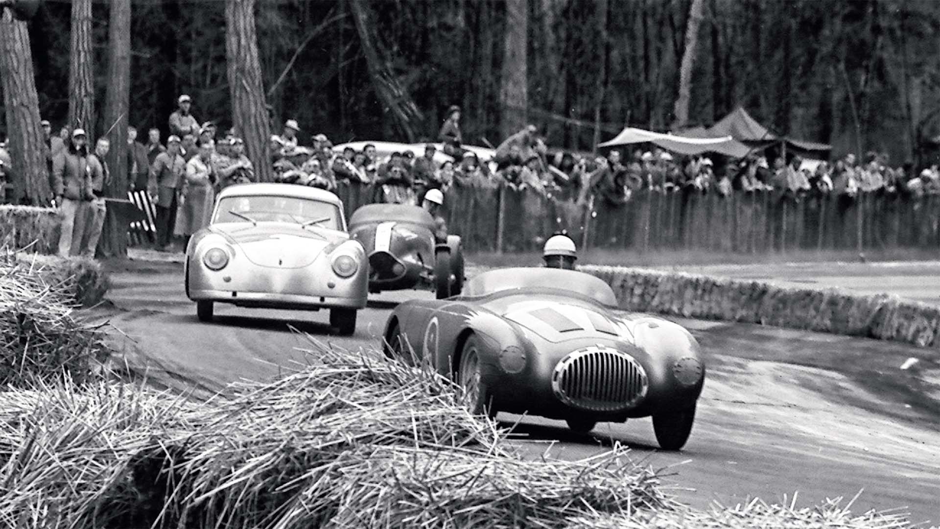 Vintage race cars on a track with spectators in the background